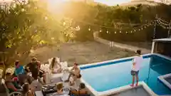 A group of friends relaxing around an outdoor backyard swimming pool at sunset.