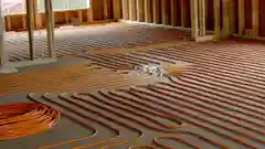 Orange hydronic heating pipes installed under subfloor during construction.