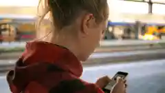 Close-up of a woman checking her smartphone while waiting at a train platform.