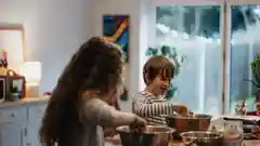 A young girl and a young boy standing together in a home kitchen.