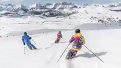 Three people in colorful ski gear skiing down a sunny, snow-covered mountain slope.