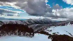 Snow-covered mountain peaks under a bright, cloudy blue sky in an alpine landscape.