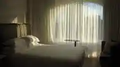 A bedroom with a large arched window, sheer white curtains, a bed with white bedding, and a cozy armchair.