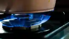Blue flame burning on a gas stove burner under a cooking pot.