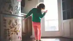 A child dancing in front of a refrigerator covered in magnets in a brightly lit kitchen