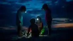 Three children wearing headlamps playing in the sand on a beach at dusk or during the night.