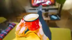 A person relaxing on a couch, holding a red mug while enjoying a warm drink in a cozy living room setting.