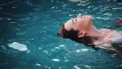 Woman floating on her back in a clear blue swimming pool.