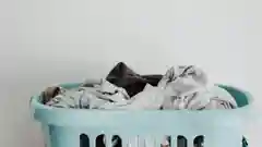 An overflowing light blue laundry basket containing crumpled and folded clothes.