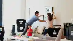A family of three happily hanging a picture frame on a wall in a room filled with moving boxes.