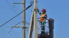 A line worker in safety gear working on a utility pole with power lines against a clear blue sky.