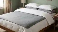 A gray electric blanket laid across a made bed with white sheets.