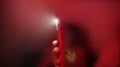 A hand holding a red smartphone with its flashlight turned on in a dark, red-lit room.