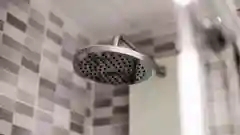 A modern, chrome water-saving shower head mounted in a clean, contemporary bathroom.