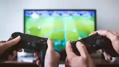 Close-up of two people holding black video game controllers while playing a soccer game.