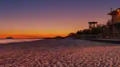 A glowing neon logo sign showing the Australian Made and Grown logo sits on the beach at sunset hour.