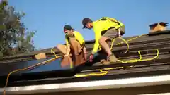 Two technicians wearing safety harnesses installing solar panels on a residential roof.