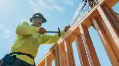 A construction worker wearing a hard hat hammers wooden framing on a house building site.