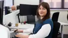 A smiling woman sits in an office at her desk with a smile on her face.