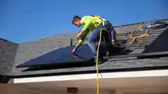 A technician wearing a safety harness installing solar panels on a residential roof.