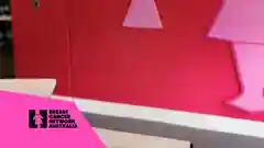 A woman sits in front of a pink wall