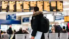 A traveler stands in an airport terminal, looking up at the flight information display board.