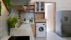 Bright modern kitchen with light wood cabinets, white tile backsplash, a front-loading washer, green pothos plant, and stainless-steel refrigerator