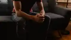 Person on sofa in a dimly lit room with hands clasped on their lap