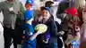 A smiling child in a blue sports uniform holds a football, surrounded by other kids and adults at a team meet-and-greet event.