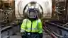 Worker in yellow hi-vis jacket and full-face safety visor standing inside an underground tunnel construction zone