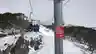 A chairlift carries skiers above a snowy slope, with a Red Red Energy sponsorship sign attached to the lift tower.