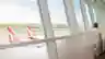 A woman sitting in an airport lounge holding a coffee cup, gazing out floor-to-ceiling windows at Qantas planes on the tarmac.