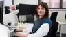 A smiling woman sits in an office at her desk with a smile on her face.