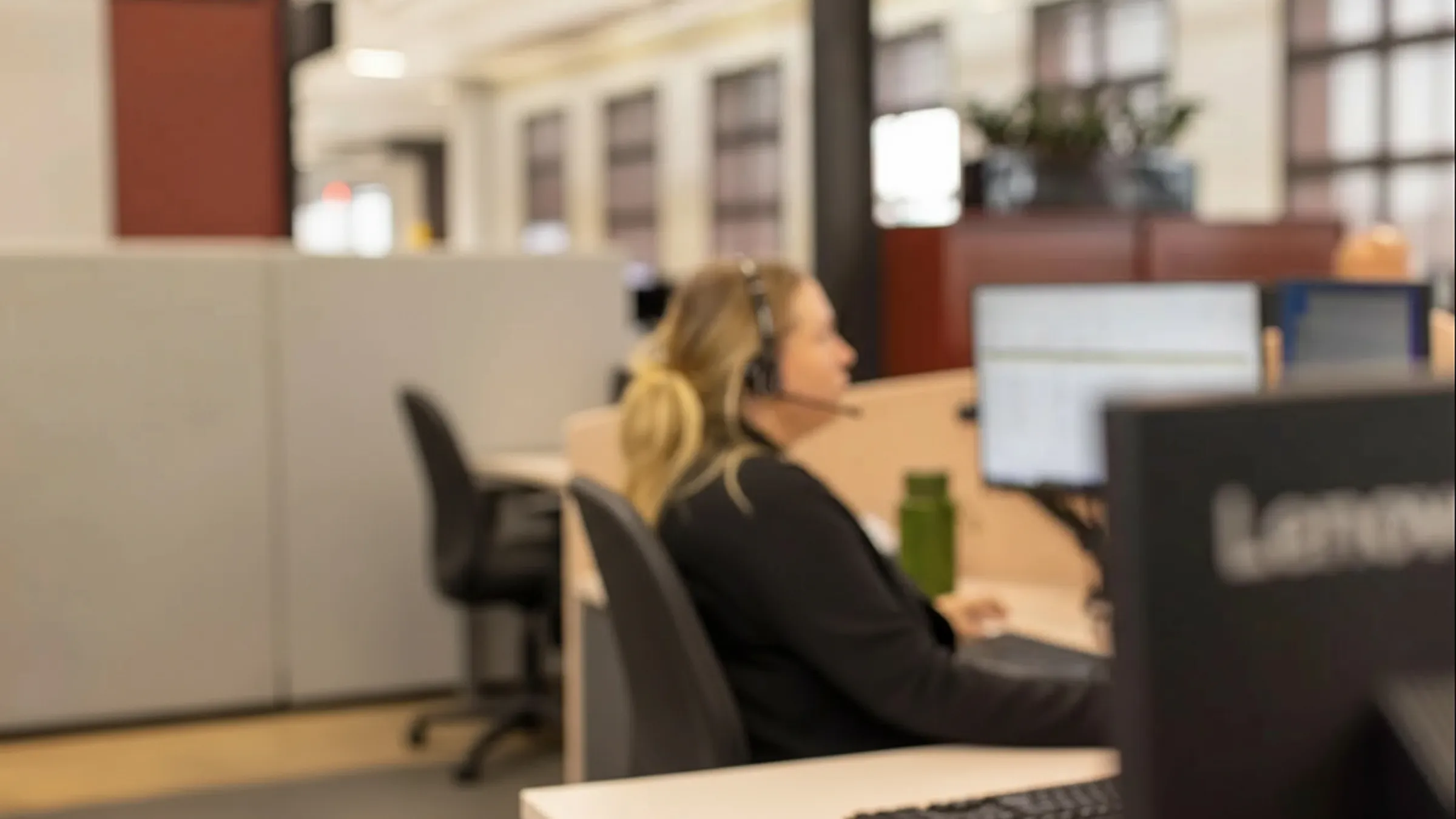 A man smiling warmly at the camera while wearing a telephone headset. He sits in a call center setting, looking friendly and approachable.