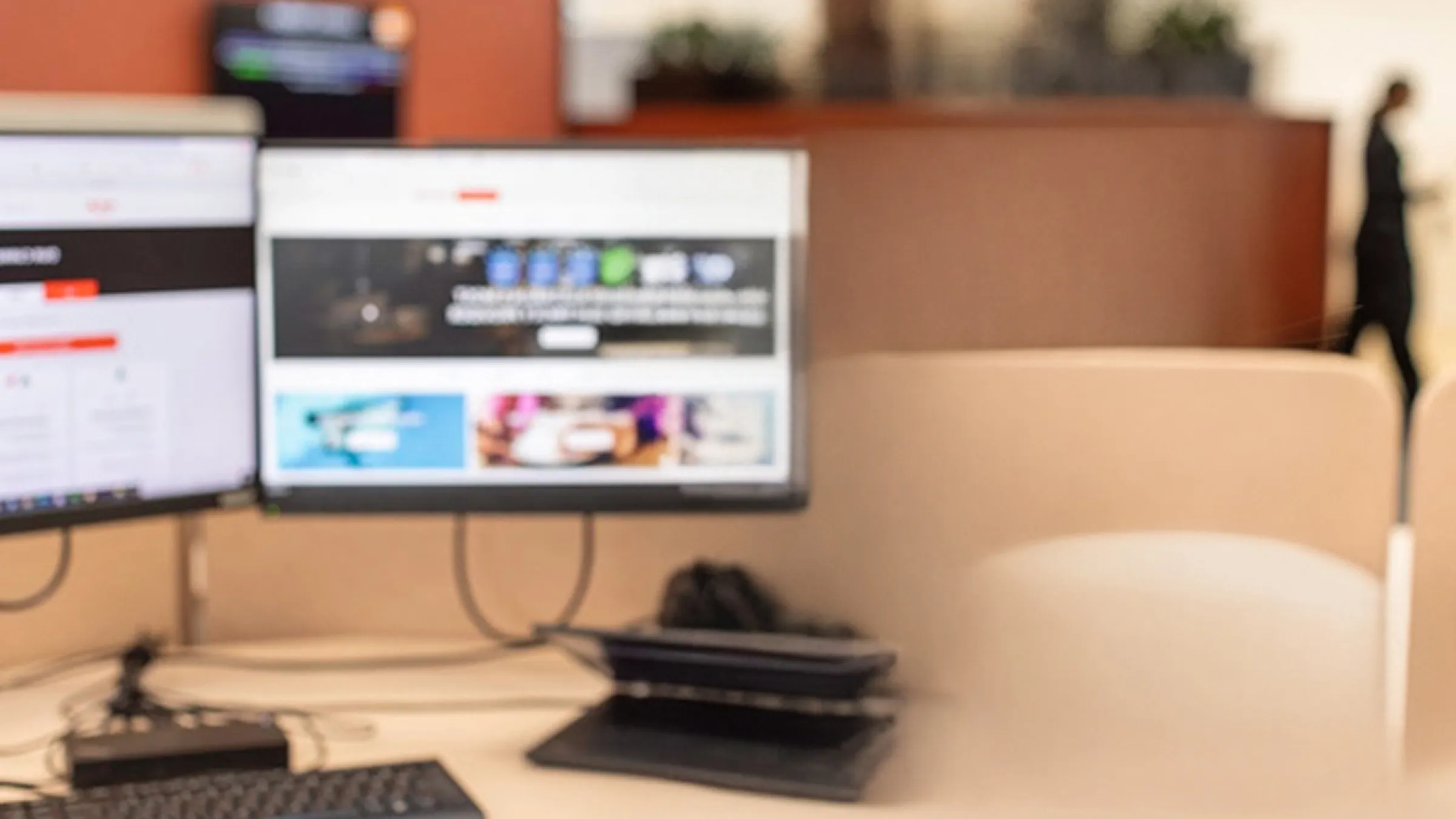 A young woman with curly hair wearing a grey shirt sits by a computer in an office building. She has a headset on as she prepares to answer a call.