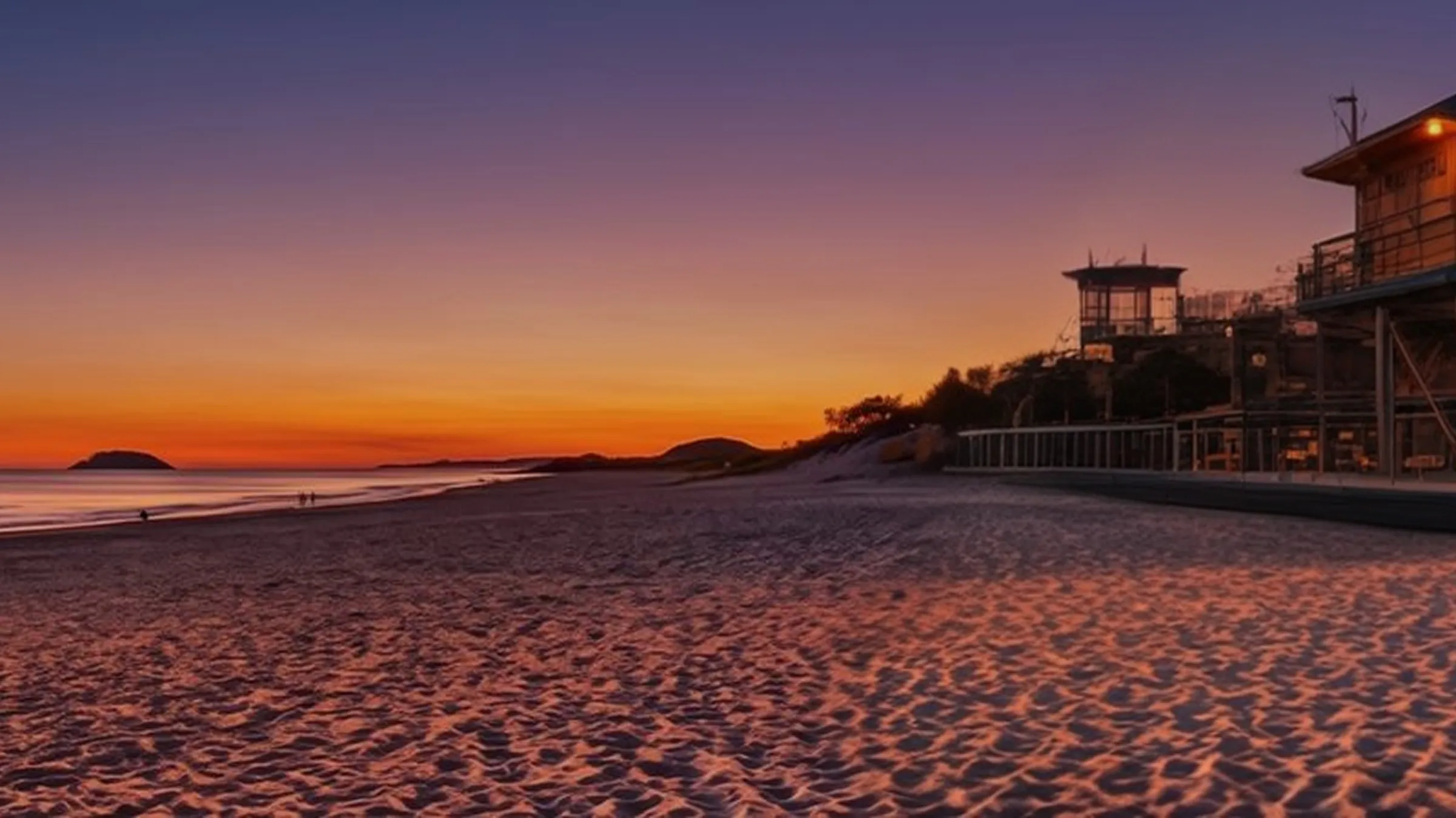 A glowing neon logo sign showing the Australian Made and Grown logo sits on the beach at sunset hour.